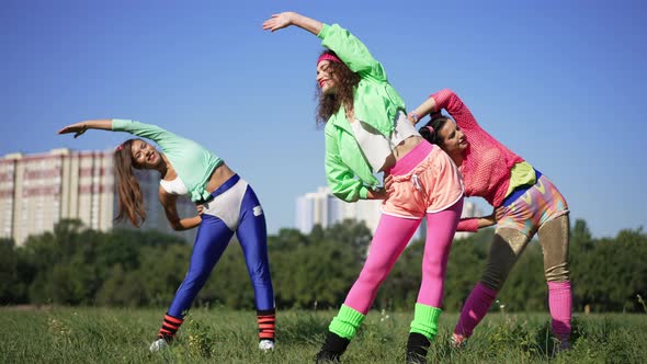 Portrait of Three Fit Caucasian Retro Sportswomen Bending Warming Up in Sunlight Outdoors on Green