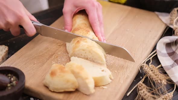 Woman Slicing Fresh Baguette Bread on Wooden Cutting Board