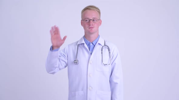 Happy Young Blonde Man Doctor Waving Hand