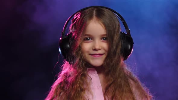 Little Girl in Headphones Dancing on Smoky Background, Slow Motion alt
