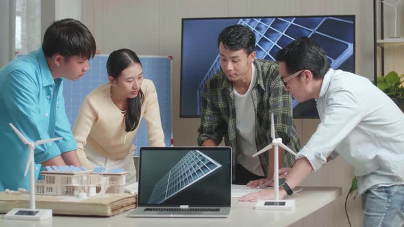 Laptop Showing Solar Cell While Asian Engineers Group Discussing About Work On The Blueprint