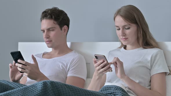 Attractive Couple Sitting in Bed and Using Smartphone