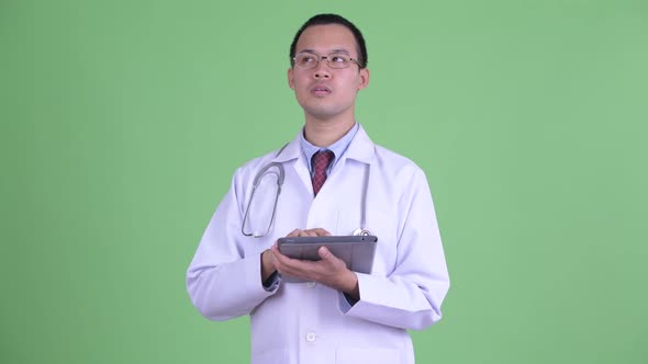 Happy Asian Man Doctor Thinking While Using Digital Tablet