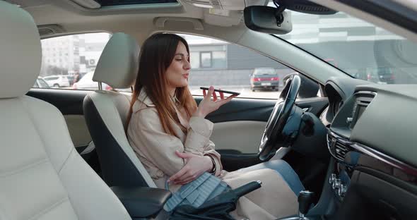 Smiling Positive Brunette Woman Sitting in Car Giving Commands to Voice Assistant Living Voice