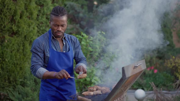 Confident Concentrated African American Man Taking Off Grilled Burger Patties From Barbecue Grid