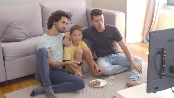 Happy Gay Parents and Son Eating Cookies and Watching Movie