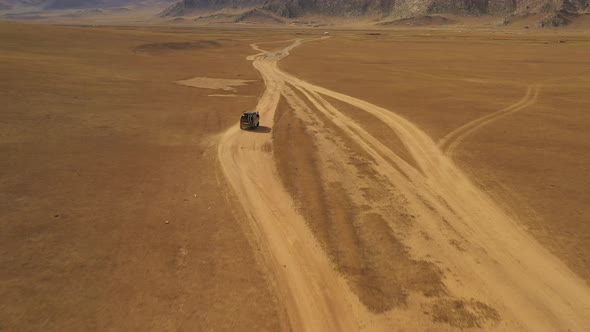 Aerial dolly of van driving through steppe on dust road towards mountains in daytime, Mongolia