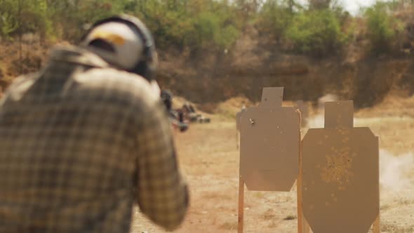 Caucasian Male in Plaid Shirt with Headphones Shooting at Targets with Airsoft Gun Outoddrs in