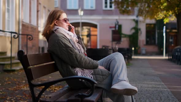 Woman Have a Talk By Smartphone Sitting on the Bench in the Street of Old Town  60p