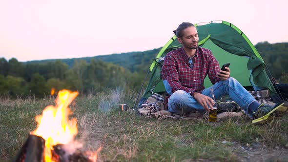 Man Traveling In Nature, Sitting Near Camp With Phone And Beer