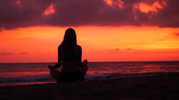 Young Girl Meditating on the Beach Looking on Ocean Waves Silhouette Against Amazing Sunset
