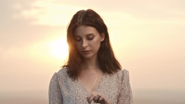 A Young Woman Artist Standing at Sunset Holding Painting Palette Bites the Brush and Putting Her