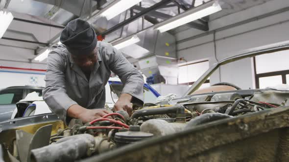 African American male car mechanic screwing screws in a car engine