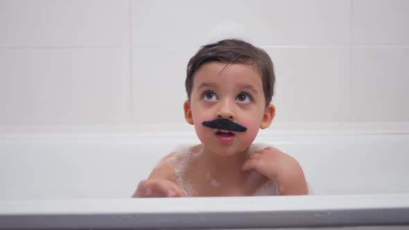 Small Boy with a Black Mustache Sits in the Bathroom