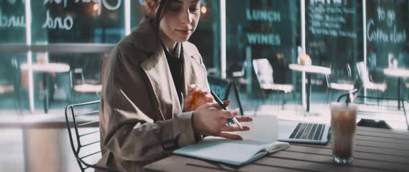 Young business woman sitting with a laptop and making notes in notebook