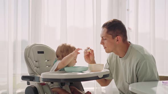 Father Acting Mom Feeding His Son Baby 1 on Chair in the House