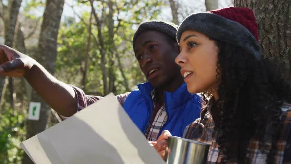 Smiling diverse couple checking map and hiking in countryside