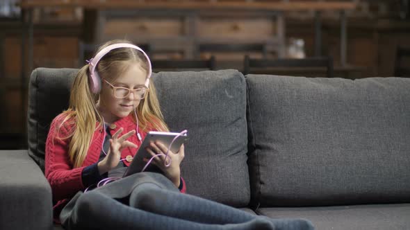 Cute Girl in Headphones Using Touchpad on Sofa