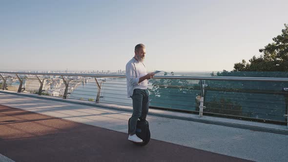 Elderly Man Reads Report Riding Electric Unicycle in Morning