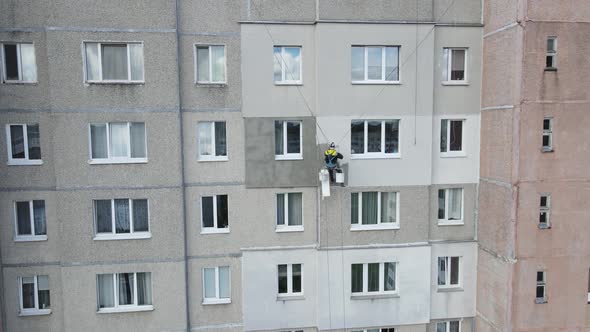 An Industrial Climber Suspended on Ropes and Paints the Wall of a Building with a Roller