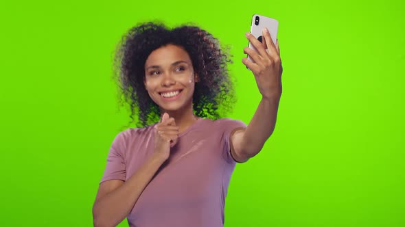 Glad black woman smiles broadly, takes selfie portrait on white cell phone