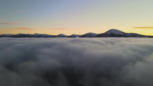 Aerial View of Vibrant Sunrise Over White Dense Clouds with Distant Dark Mountains on Horizon