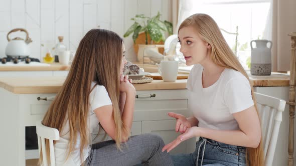 Serious Mother Blonde Caucasian Woman with Long Hair Sits on Chair in Modern Kitchen with Daughter