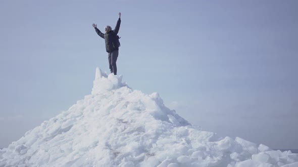 Emotional Happy Man in Warm Coat Standing on the Top of Glacier Throwing Up His Hands, Triumphing