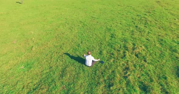 Low Orbital Flight Around Man on Green Grass with Notebook Pad at Yellow Rural Field