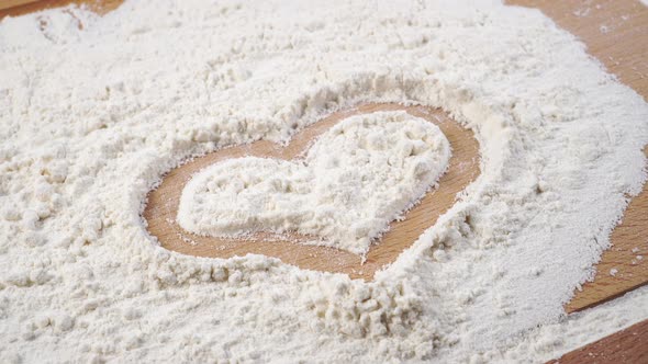 Heart symbol are drawn on flour on a cutting wooden board.