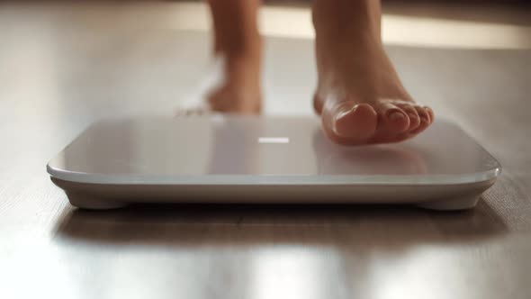 Girl Legs Step On Bathroom Weight Scale. Diet Female Feet Standing Weighing Scales On Room.