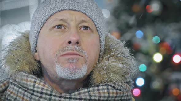 A Hungry Elderly Man Eats in a Food Court at a Christmas Market on the Street in Winter