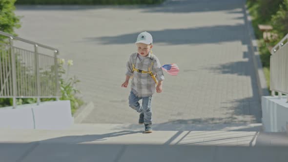 Child Boy Kid in Blue Cap Yellow Backpack and Waving USA Flag Walking Upstairs