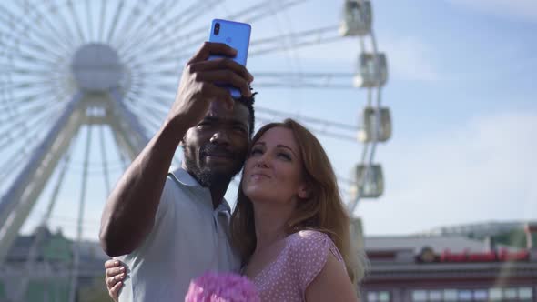 Young Couple Makes Selfie on the Background of a Ferris Wheel