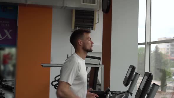 Slow Motion of a Young Man Running on Treadmill in Fitness Center. Side View. 