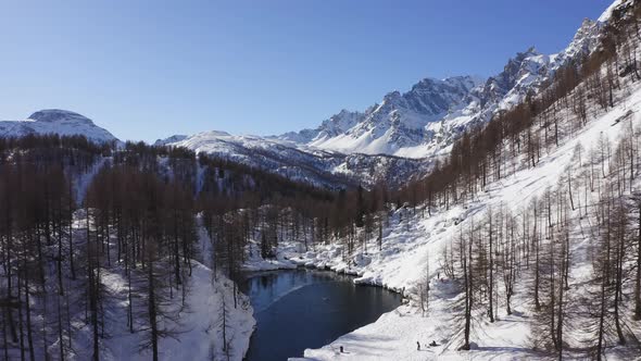 Aerial Over Blue Alpine Lake Revealing Snowy Mountain Valley in Sunny Winter Day