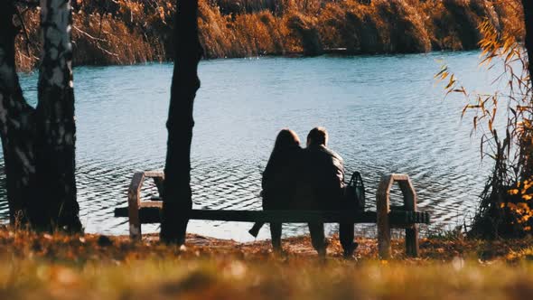 Young Romantic Couple Sitting on a Bench in an Autumn Park By the River