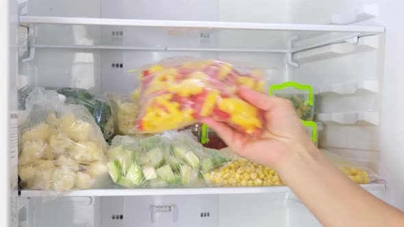 Female Hands puts bags of frozen vegetables in the fridge.