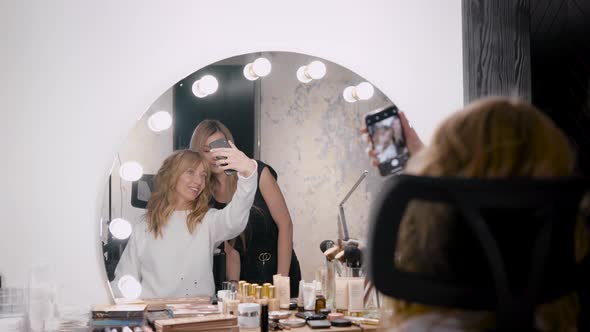 Female Client of Beauty Shop Is Taking Selfie with Professional Makeup Artist in Front of Mirror