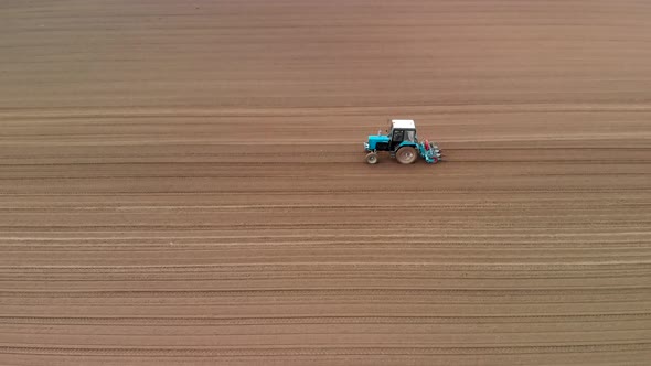 A Blue Tractor Works in the Spring Against the Background of a Huge Brown Field, with a Precise