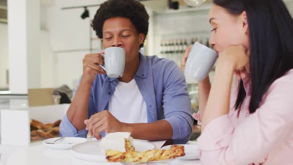 Video of happy diverse woman and man drinking and talking at coffee shop