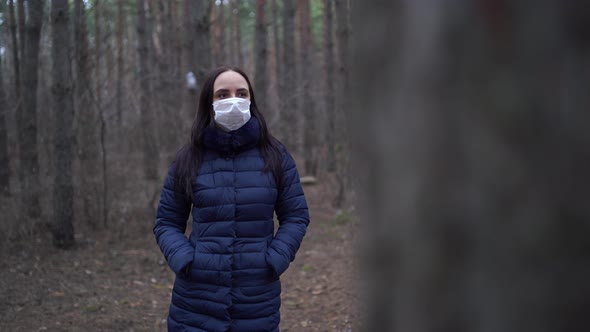 Portrait of Young Woman in Medical Mask on Her Face Leaning on Tree in Forest