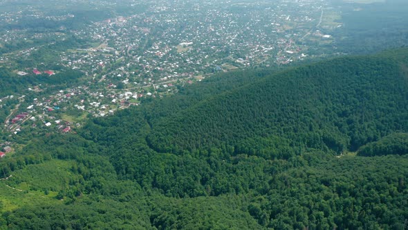 Aerial View of the Village in the Valley Behind the Mountains Covered with Dense Green Forest