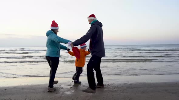 Happy Mom, Dad and son dance on the beach in Christmas hats