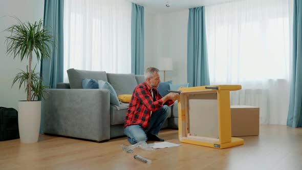 A Man in Home Clothes Assembles a Soft Chair Himself