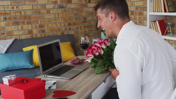 Caucasian man making video call using laptop holding bunch of flowers and blowing kiss