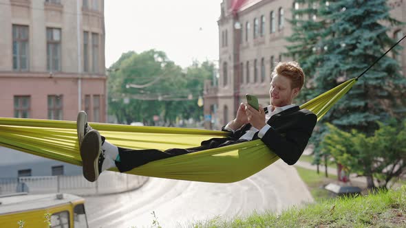 Happy Guy in Suit Resting in Hammock and Using Mobile