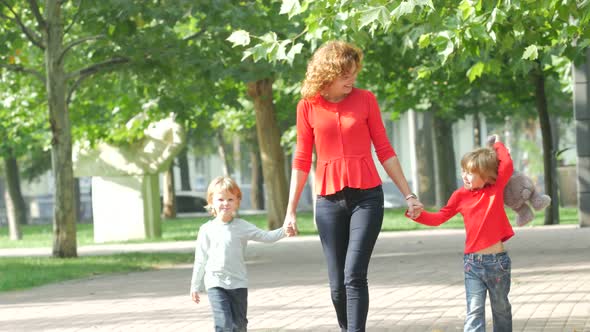 Mother and Two Young Children Walking on Path Holding Hands Smiling