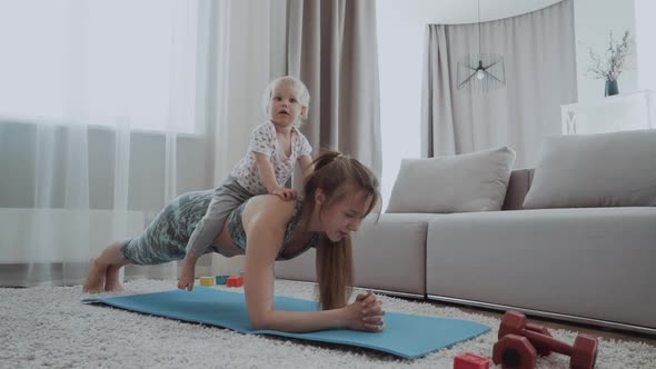 Mother and the Little Baby are Engaged in Yoga in Sportswear at Home