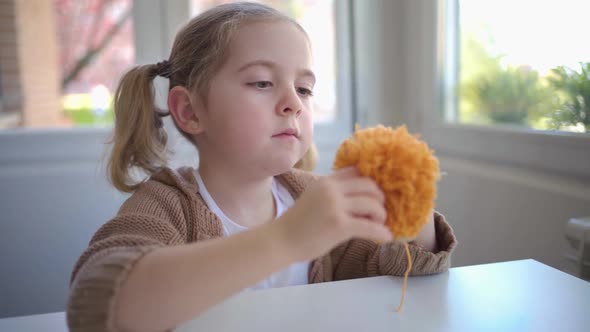 Concentrated little girl in process of making handmade pompom in morning kitchen